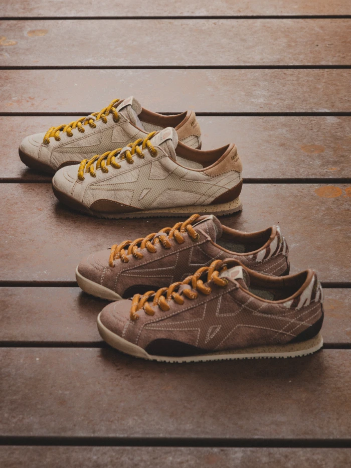 Low-top beige and brown leather and suede sneakers with mustard yellow laces on wooden planks