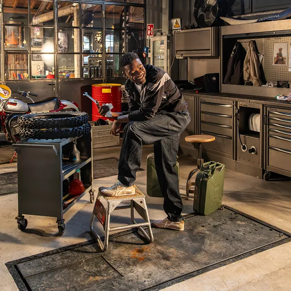 Man in a motorcycle workshop wearing Americanino casual sneakers, representing rugged urban lifestyle and everyday comfort.