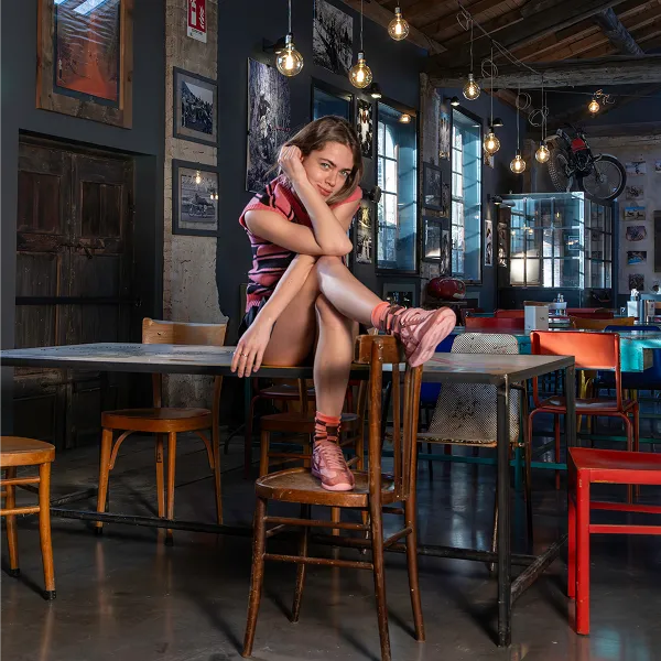 Woman sitting on a chair in a stylish urban café wearing pink Americanino casual sneakers, showcasing modern women’s lifestyle footwear.